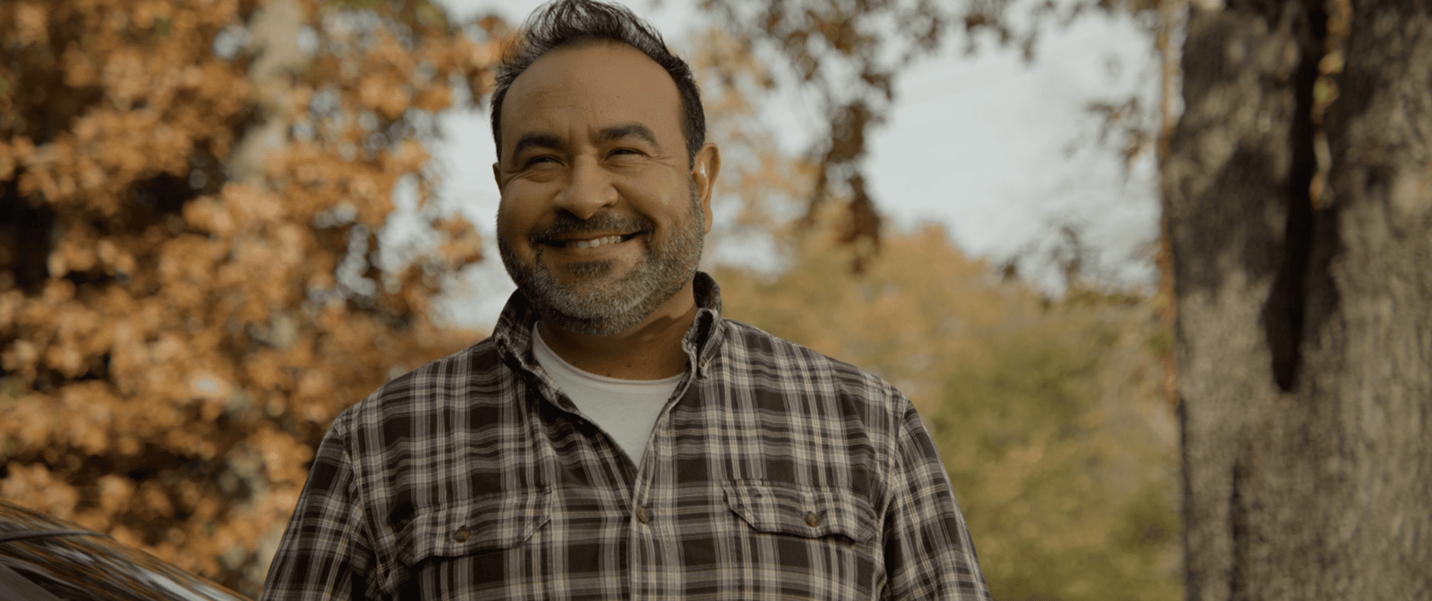 A happy man looks beyond the camera surrounded by autumn trees in a production still from the motion picture "Porch Pirates" produced in association with Tame Rabbit.