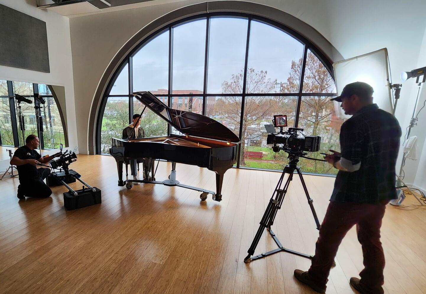 Two camera people video a man sitting at a piano for a music video.